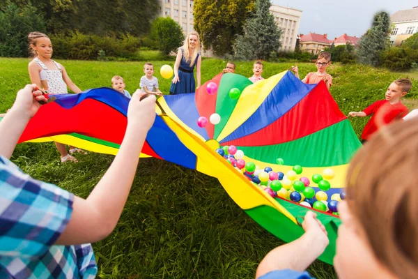 A gyerekek szivárvány ejtőernyőt tartanak színes golyókkal. — Stock Fotó