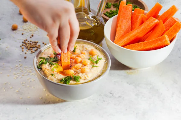 Mano delle donne immergendo carota in hummus diffusione — Foto Stock