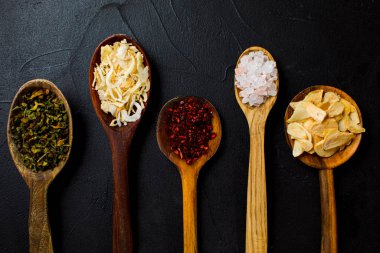 Siyah arka planda tahta kaşıklarda çeşitli baharatlar.