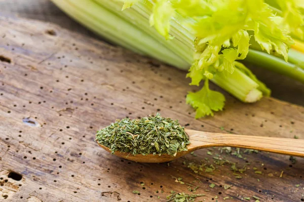 Apio verde seco en una cuchara de madera y apio fresco en una mesa de madera — Foto de Stock