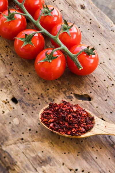 Ramo de tomate cereja e colher de madeira preenchida com tempero de tomate seco — Fotografia de Stock