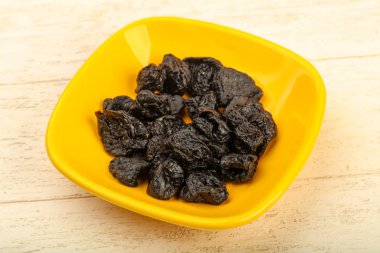 Kurumuş erikler ahşap arka planda kasede yığılıyor.