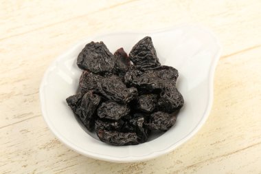 Kurumuş erikler ahşap arka planda kasede yığılıyor.