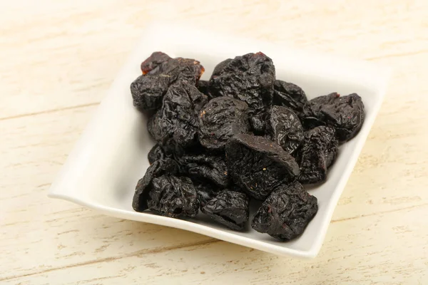 Kurumuş erikler ahşap arka planda kasede yığılıyor.