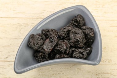 Kurumuş erikler ahşap arka planda kasede yığılıyor.