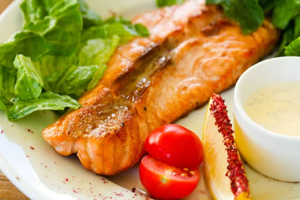 Grilled salmon steak with sauce and salad leaves