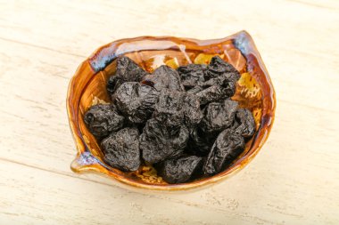 Kurumuş erikler ahşap arka planda kasede yığılıyor.