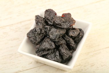 Kurumuş erikler ahşap arka planda kasede yığılıyor.