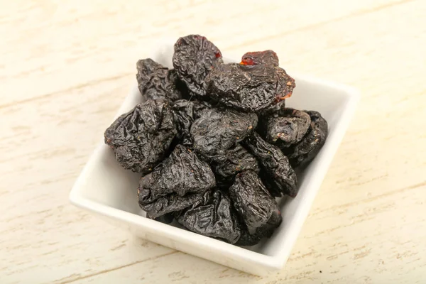 Kurumuş erikler ahşap arka planda kasede yığılıyor.