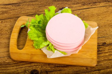 Sliced sausage with salad leaves over the wooden background clipart
