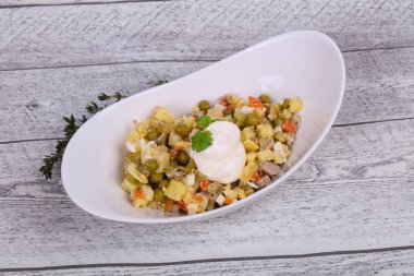 Geleneksel Rus salatası, ahşap arka planda beyaz kasede tavuk var.