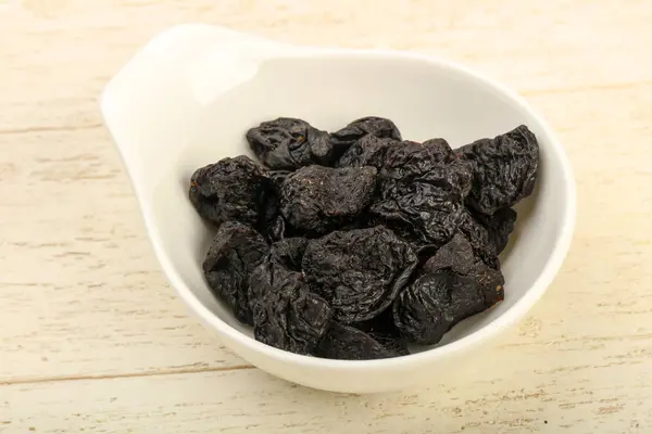 Dried plums heap in the bowl over wooden background