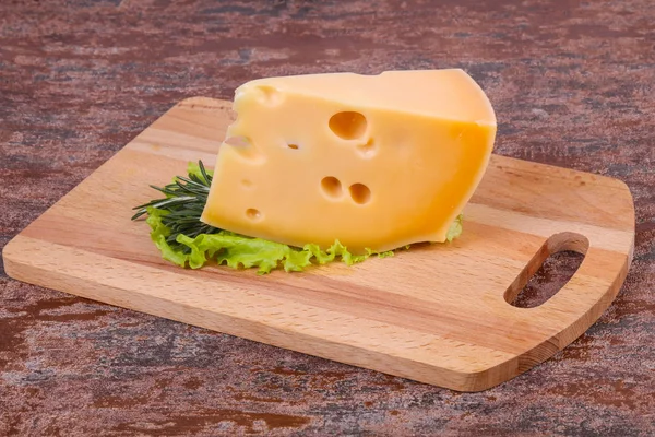 Maasdam cheese on the board served salad leaves and rosemary
