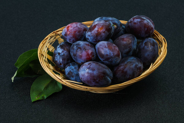 Спелые сливы в корзине с листьями