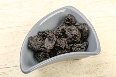 Kurumuş erikler ahşap arka planda kasede yığılıyor.