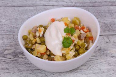 Geleneksel Rus salatası, ahşap arka planda beyaz kasede tavuk var.