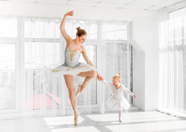 Young gorgeous ballerina with her little daughter dancing in studio