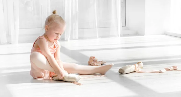 Giovane ballerina di balletto in tutù seduta sul pavimento e allacciando scarpe da punta — Foto Stock