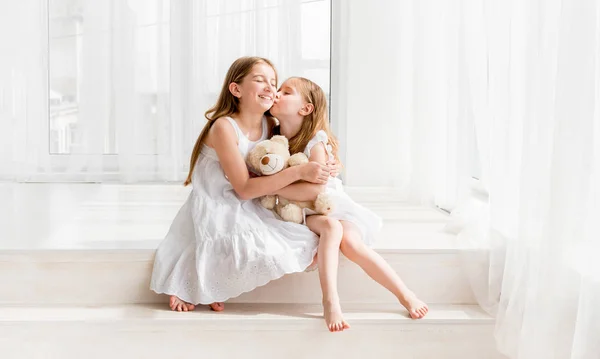 Menina beijando sua irmã mais velha enquanto sentada no chão — Fotografia de Stock
