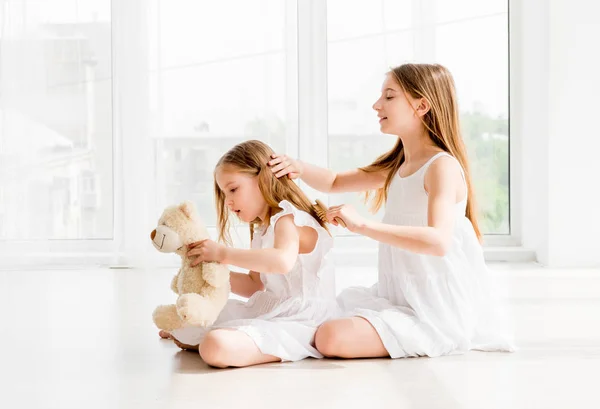 Υπέροχο κοριτσάκι βούρτσισμα τα μαλλιά της νεώτερη αδελφή — Φωτογραφία Αρχείου
