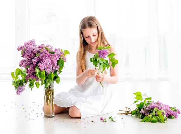 Девушка с букетом сиреневых цветов сидит на полу — стоковое фото