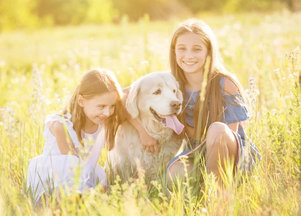 Two young girls cuddling retriever dog outdoors — Stock Photo, Image