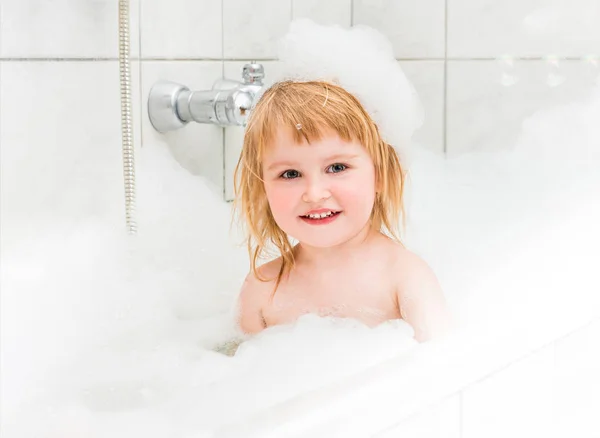 Liten flicka badar i ett badkar med skum och bubblor — Stockfoto