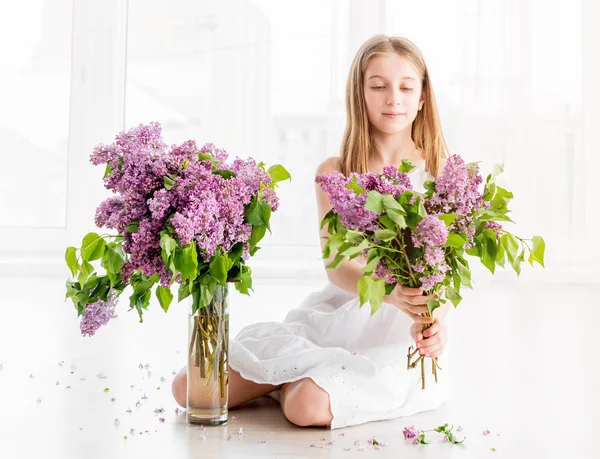 Meisje met boeket van lila bloemen zittend op de vloer — Stockfoto