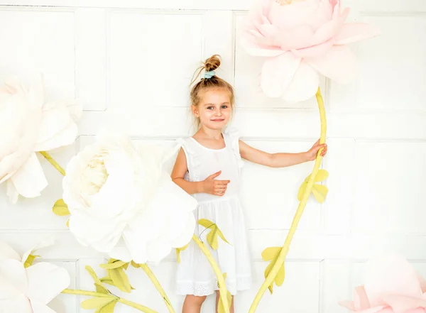 Little girl posing in studio opposite decoration with artificial flowers — Stock Photo, Image