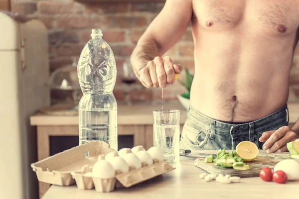 Sportlicher Mann kocht Wasser mit Zitrone in der Küche — Stockfoto