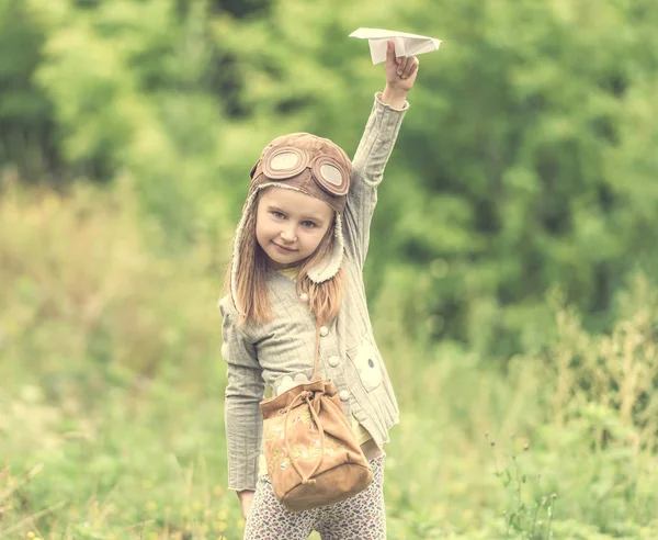 Cute little girl in helmet pilot with paper airplane — Stock Photo, Image