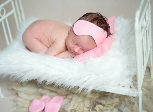 Dreamy baby girl lying curled on stomach on small crib. — Stock Photo, Image