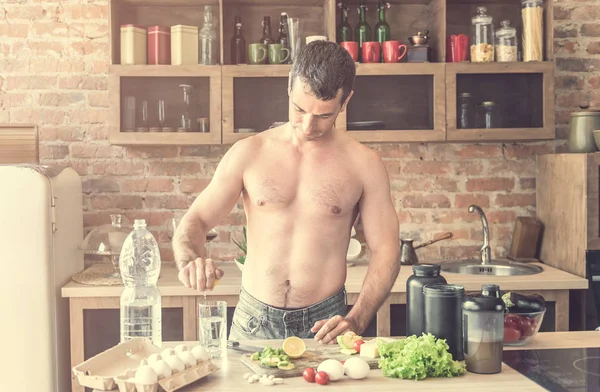 Atletický muž dělá voda s citronem v kuchyni — Stock fotografie