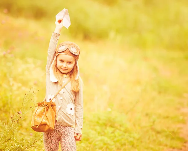 Söt liten flicka i hjälm pilot med pappersflygplan — Stockfoto