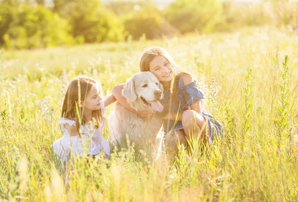 Two young girls cuddling retriever dog outdoors — Stock Photo, Image