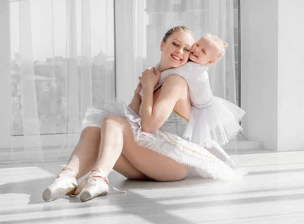 Giovane madre che abbraccia piccola figlia sorridente in studio di danza classica — Foto Stock