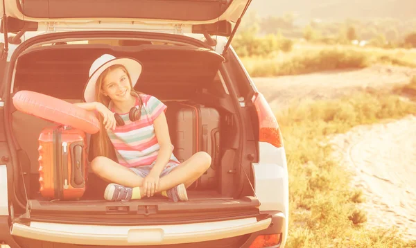 Schattig meisje in de kofferbak van een auto met koffers — Stockfoto