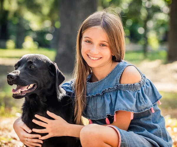 Tienermeisje zitten knuffelen van een zwarte hond in park — Stockfoto