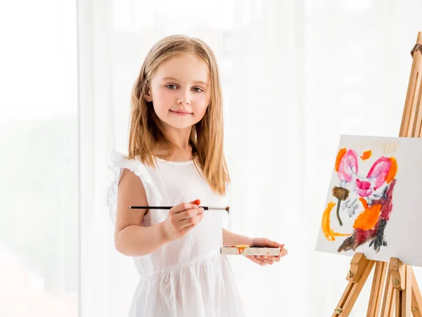 Портрет маленькой девочки, рисующей картину на мольберте — стоковое фото