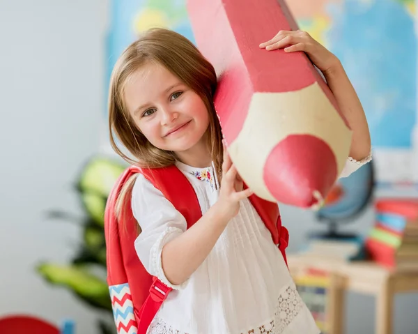 Usměvavá blonďatá holčička drží obrovský červenou tužkou v učebně školy — Stock fotografie