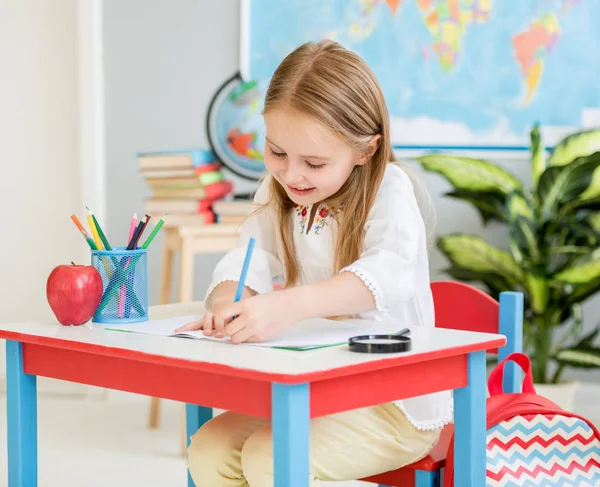 Little blond girl writing classwork in the school classroom — Stock Photo, Image