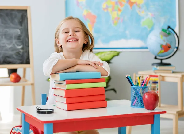 Lachende blond meisje houdt handen op de boeken in de school klas — Stockfoto