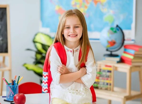 Pequena menina loira sorridente em pé na classe da escola — Fotografia de Stock