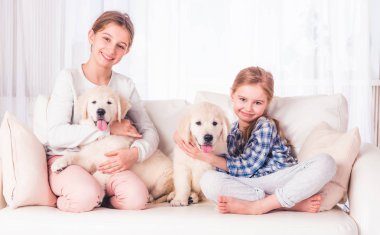 Gülümseyen kız kardeşler köpek yavrularıyla oturuyor