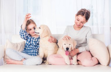 Gülümseyen kız kardeşler köpek yavrularıyla oturuyor
