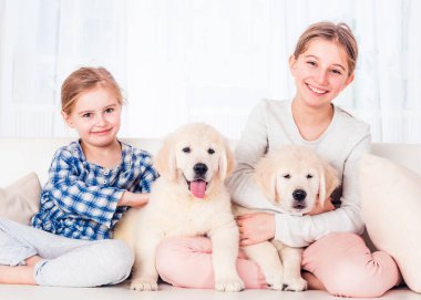 Gülümseyen kız kardeşler köpek yavrularıyla oturuyor