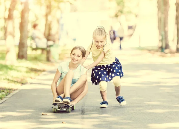 Twee zusjes spelen met een skateboard — Stockfoto