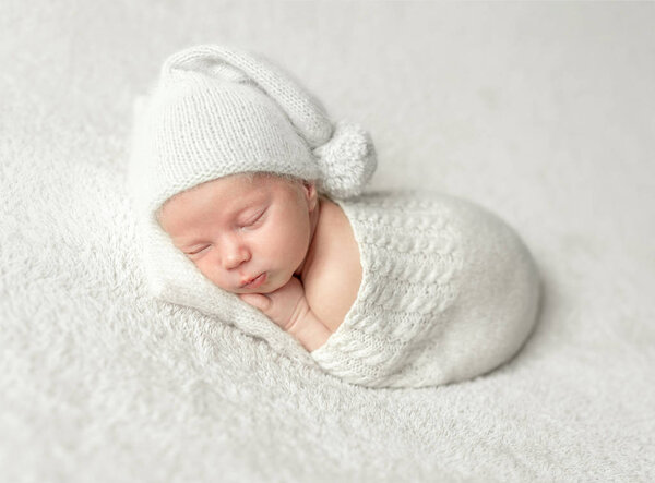 Маленький ребенок в белой вязаной шляпе и костюме, спящий
