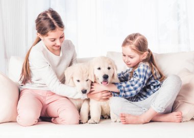 Gülümseyen kız kardeşler köpek yavrularıyla oturuyor