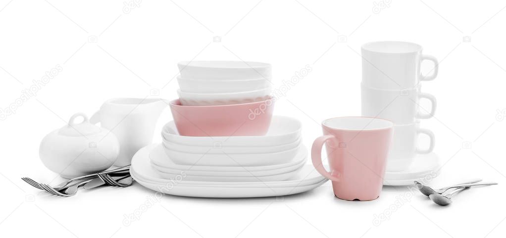 White and pink plates, sugar bowl and mugs on light background